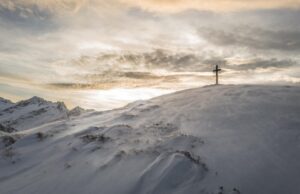 Cross on a snowy mountain summit under glowing clouds