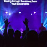 Worship crowd with raised hands under blue stage lights