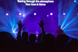 Worship crowd with raised hands under blue stage lights
